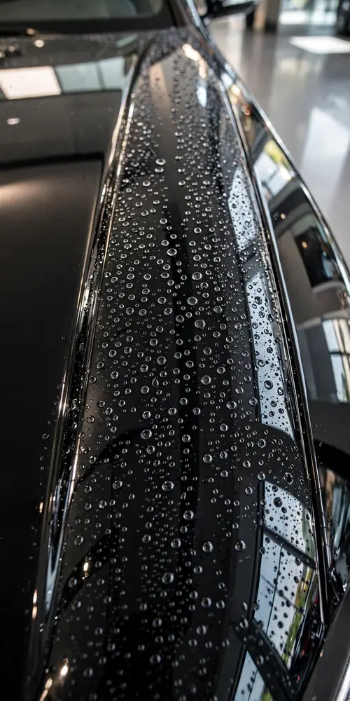 Glossy black car hood with water beading after ceramic coating