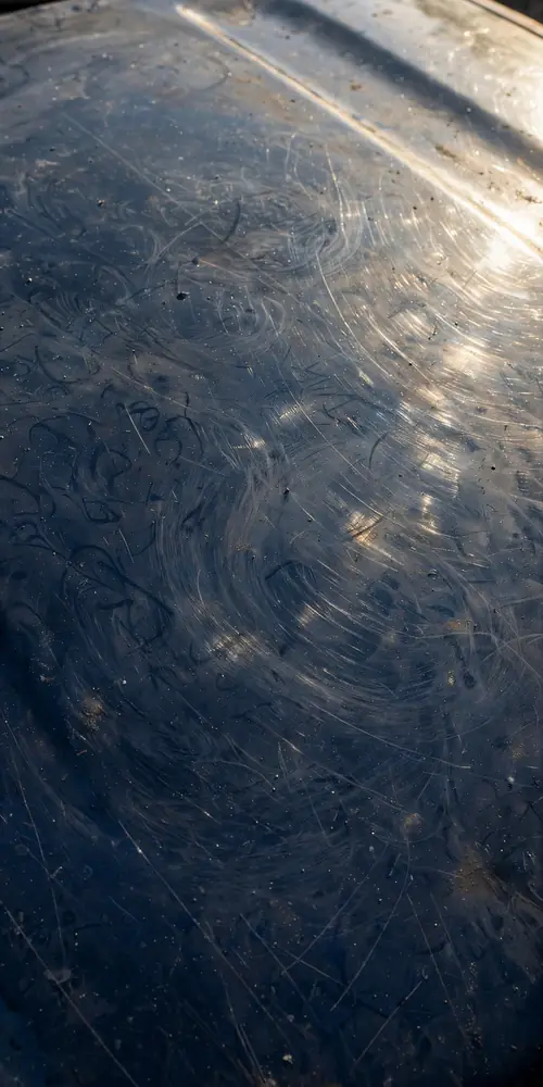 Close-up of car paint with swirl marks and light scratches in sunlight